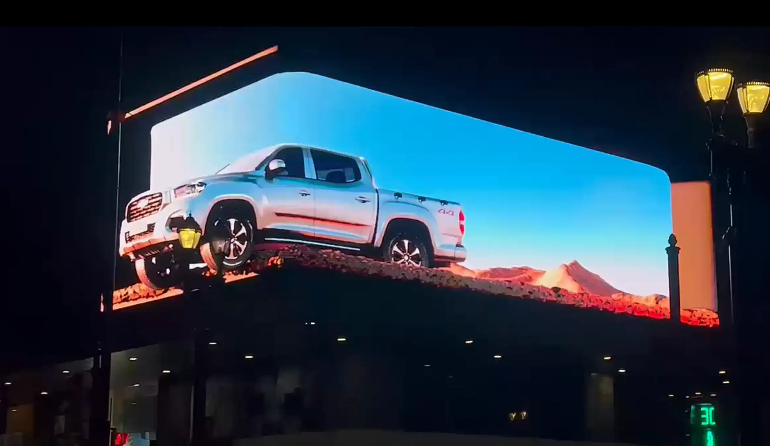 Pickup truck appearing to drive off an L-shaped anamorphic 3D billboard at night